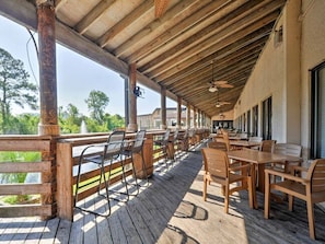 Un patio exterior cubierto con mesas y sillas de madera, una barandilla de madera y vistas del paisaje circundante.