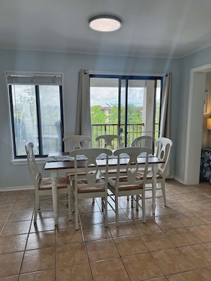 A dining area with a table and chairs, a window with curtains, and a view of greenery outside.