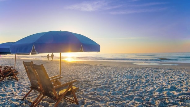 Une plage avec un grand parasol, des chaises en bois et un coucher de soleil.