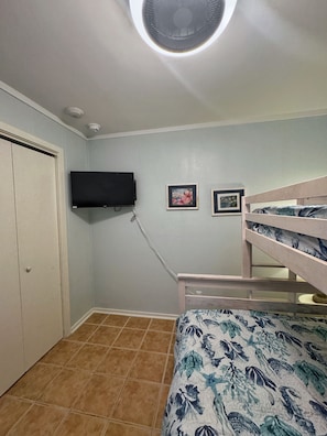 A bedroom with a bunk bed, a ceiling fan, a mounted TV, and a door.