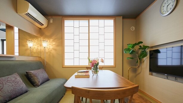 A cozy room with a wooden dining table, a green sofa, a wall-mounted TV, and a large window with a view. - 4min Shin-Okubo Sta&Very bright!/Free Wi (Shinjuku-ku)