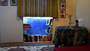 A cozy room with a bookshelf, a table with a floral tablecloth, and a window with curtains. - The Librarians' Flat (Dzveli Tbilisi)