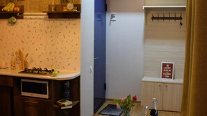 A compact kitchen with a microwave, a sink, and a stove. There is a dining table with a floral tablecloth and a vase with flowers. A clock is visible on the wall, and a sign reads "KEEP CALM CARRY ON". - The Librarians' Flat (Dzveli Tbilisi)