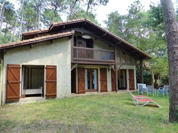 A two-story wooden house with a balcony, large windows, and a grassy yard.