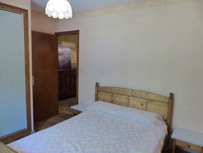 A bedroom with a wooden bed, a small bedside table, a nightstand, a door, and a mirror.