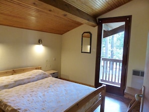 A bedroom with two beds, a wooden ceiling, a mirror, and a door leading to an outdoor area.