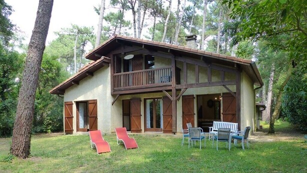 Une maison à deux étages avec un balcon, une pelouse avec des chaises et un arbre.