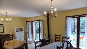 Un espace repas comprenant une table, des chaises, un lustre et une vue sur l’extérieur à travers des portes vitrées.