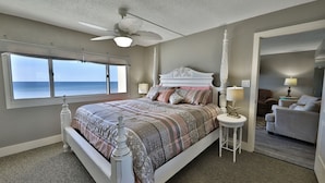 Een slaapkamer met een groot bed, een plafondventilator, uitzicht op de oceaan en een deur naar een andere kamer.