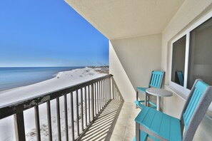 A balcony with a view of the beach, a window, and two turquoise chairs.