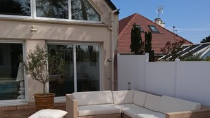 Un área exterior moderna con un amplio sofá modular, un árbol en maceta y un patio con piso de baldosas.