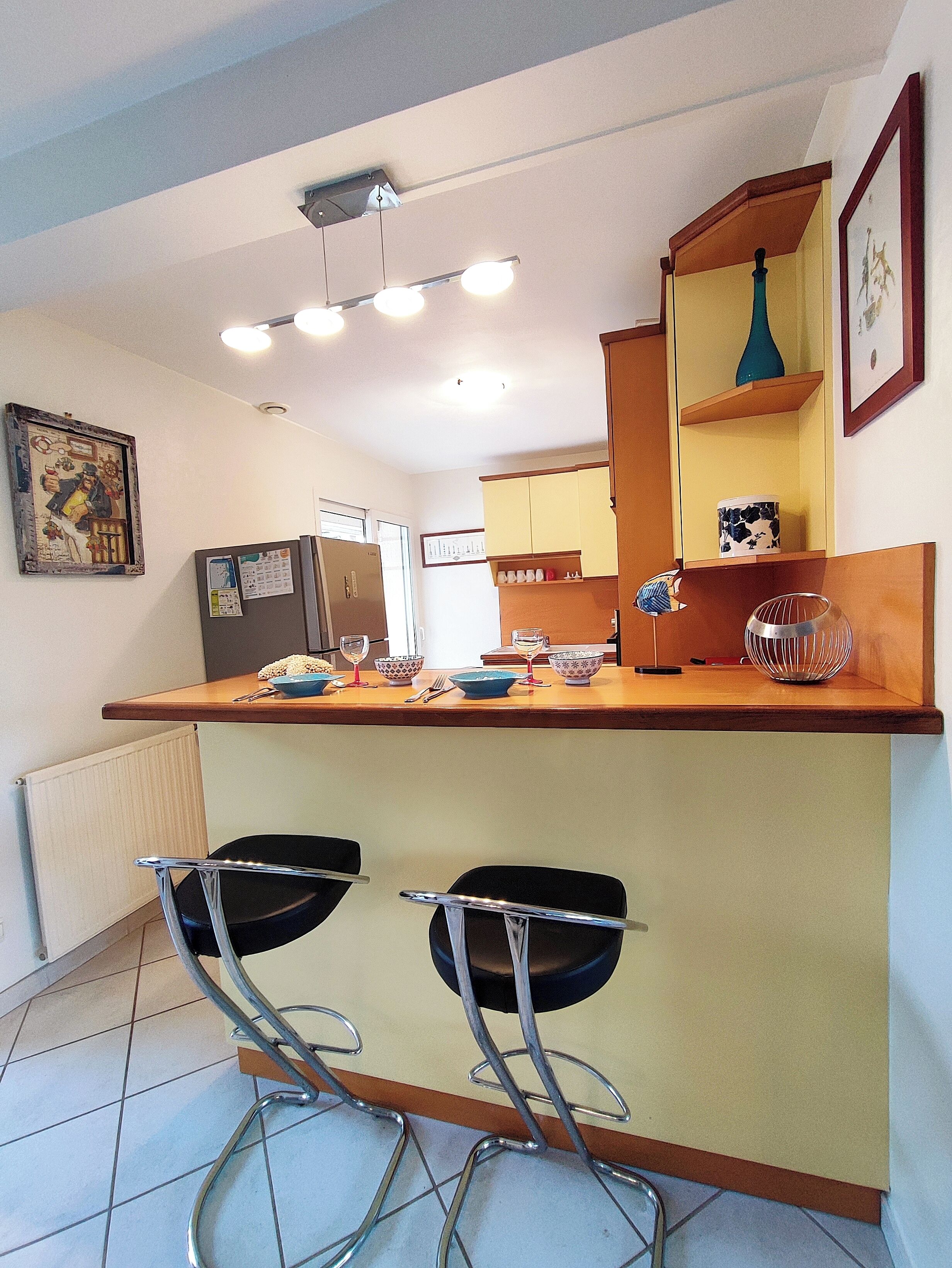 Una cucina moderna con isola centrale, due sgabelli da bar, un frigorifero e un'area pranzo con tavolo e sedie.
