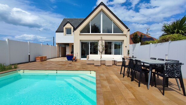 Una casa de dos pisos con piscina, mobiliario exterior y un patio trasero cercado.
