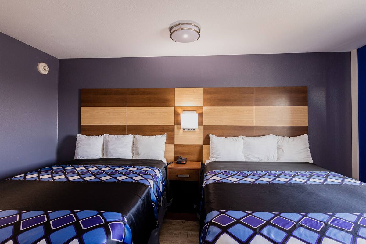 A hotel room with two beds, a wooden headboard, a nightstand with a phone, and a wall-mounted light.