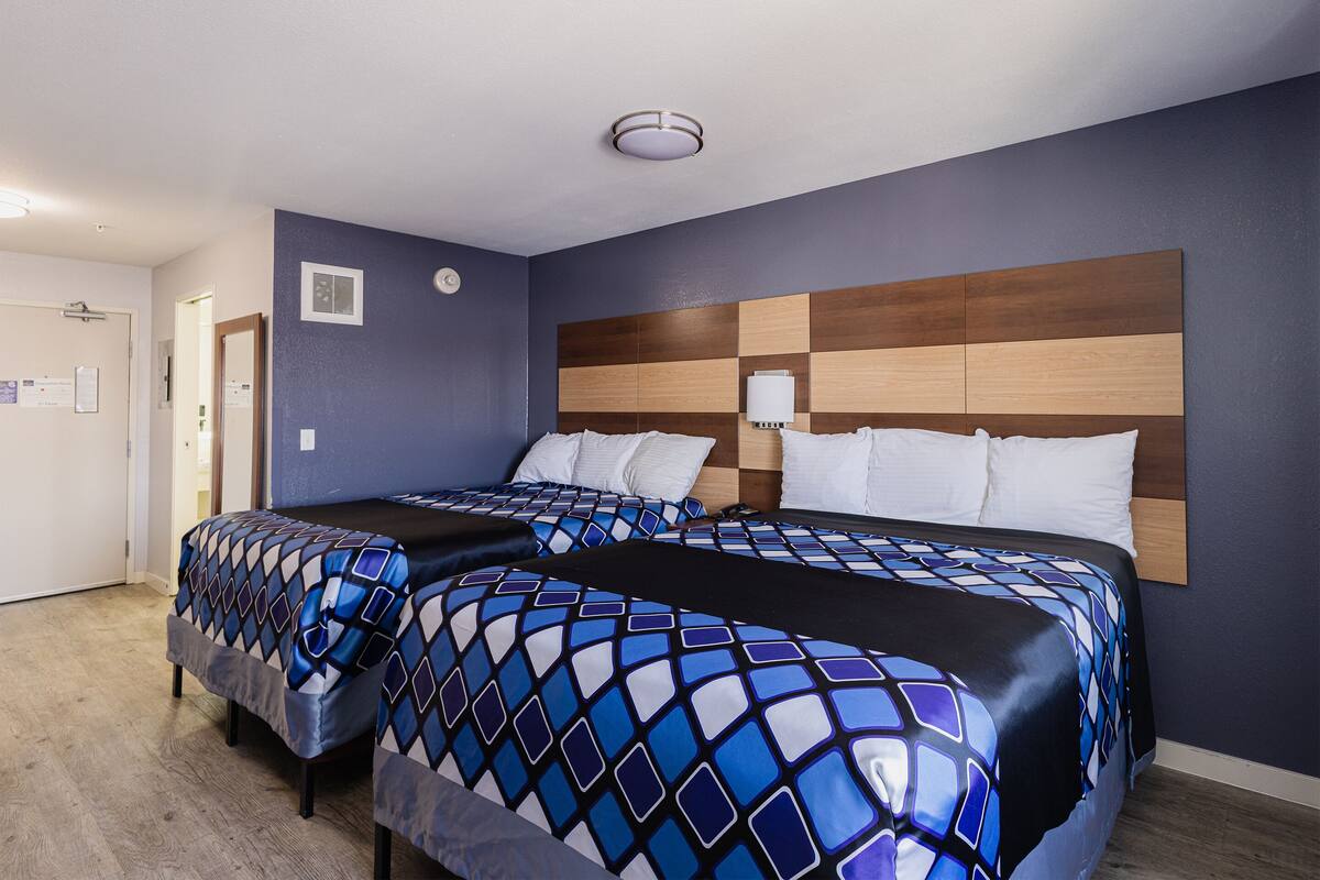 A hotel room with two beds, a wooden headboard, and a blue wall.