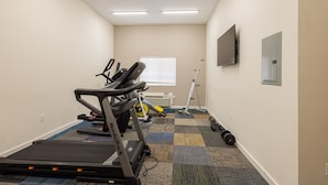 A small, carpeted room with a treadmill, elliptical, and weights.
