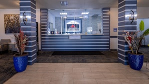 A reception area with a modern design, featuring a reception desk, a welcome screen, and two large potted plants.