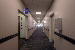 Pasillo de hotel con letreros indicativos para servicios de huéspedes, un ascensor y un detector de incendios.