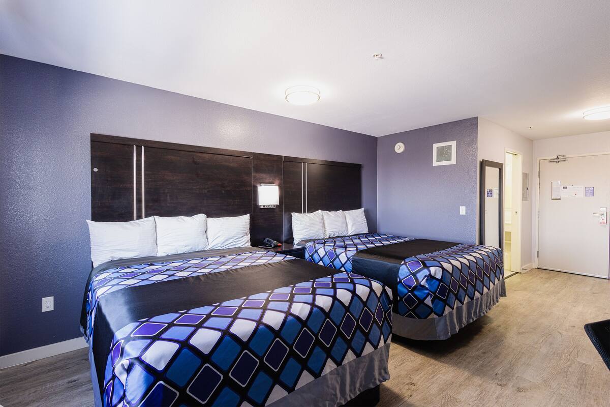 A hotel room with two beds, a dark headboard, and a small window.
