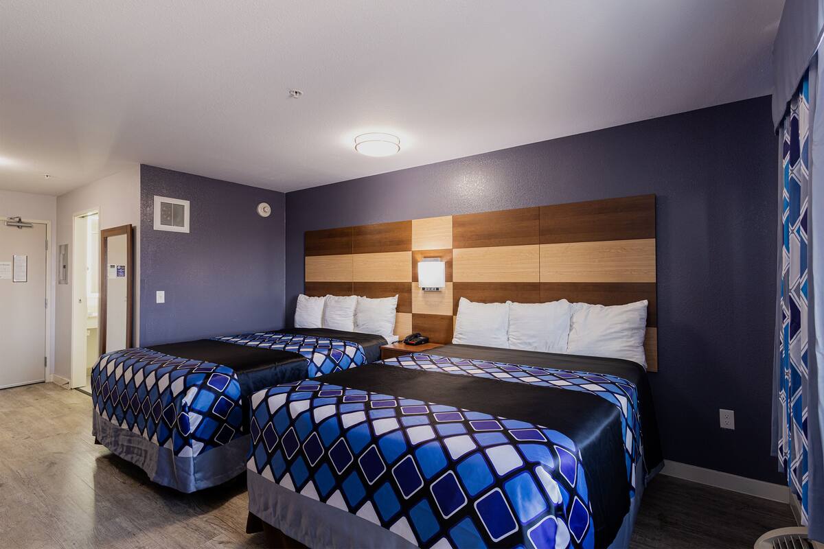 A hotel room with two beds, a wooden headboard, and a nightstand with a lamp.