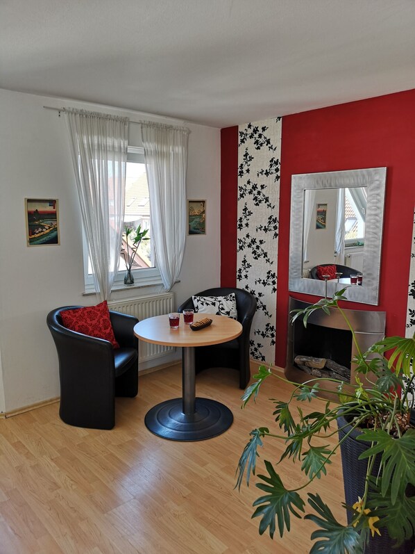 A living room with a round table, two black leather chairs, a red wall, a large mirror, and a potted plant. - Whole house-120sqm rest oasis near Berlin (S-Bahn close) (Panketal)