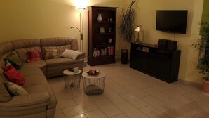 Un salon avec un canapé, une bibliothèque, un téléviseur et une petite table ronde.