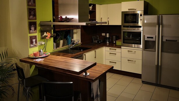 Une cuisine équipée d’une table en bois, d’un évier et d’appareils électroménagers en acier inoxydable, notamment un four à micro-ondes et un réfrigérateur.