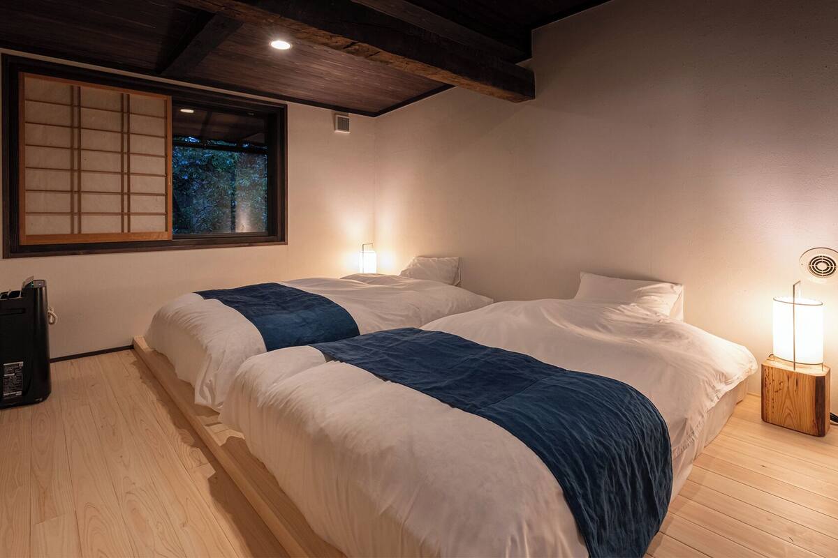 A room with two beds, a window with a view, a bedside table with a lamp, and a speaker.