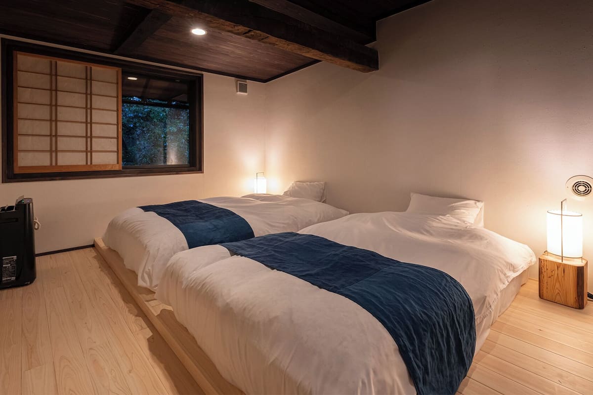 Una habitación con dos camas, una ventana con vistas, una mesita de noche con lámpara y un altavoz.