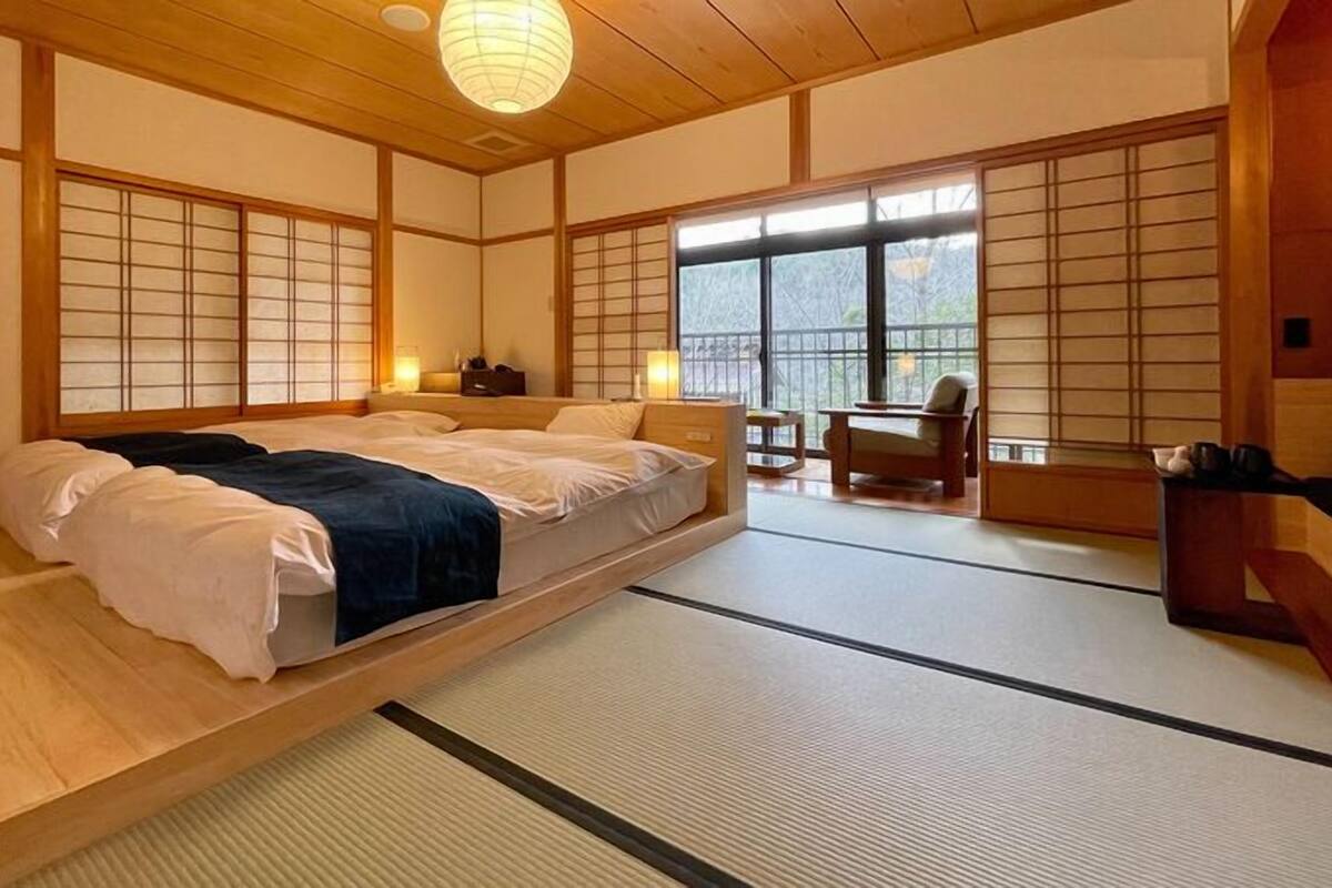 A traditional Japanese-style room with tatami flooring, a low platform bed, sliding shoji doors, and a view of the outdoors.