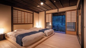 A traditional Japanese-style room with tatami flooring, a low wooden bed, sliding shoji doors, and a view of a forest.