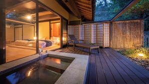 A spa area with a hot tub, a wooden deck, and a room with a bed and sliding glass doors.