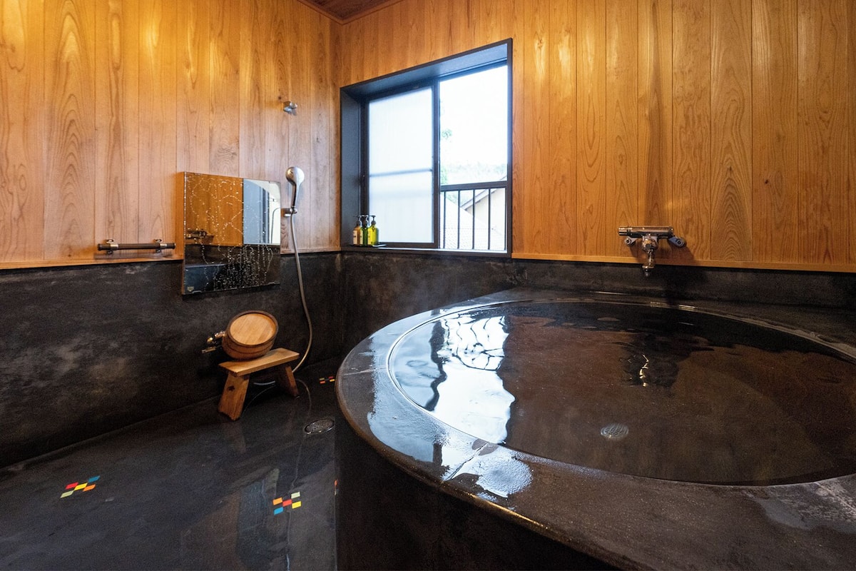 A wooden interior with a large bathtub, a wooden stool, and a window.
