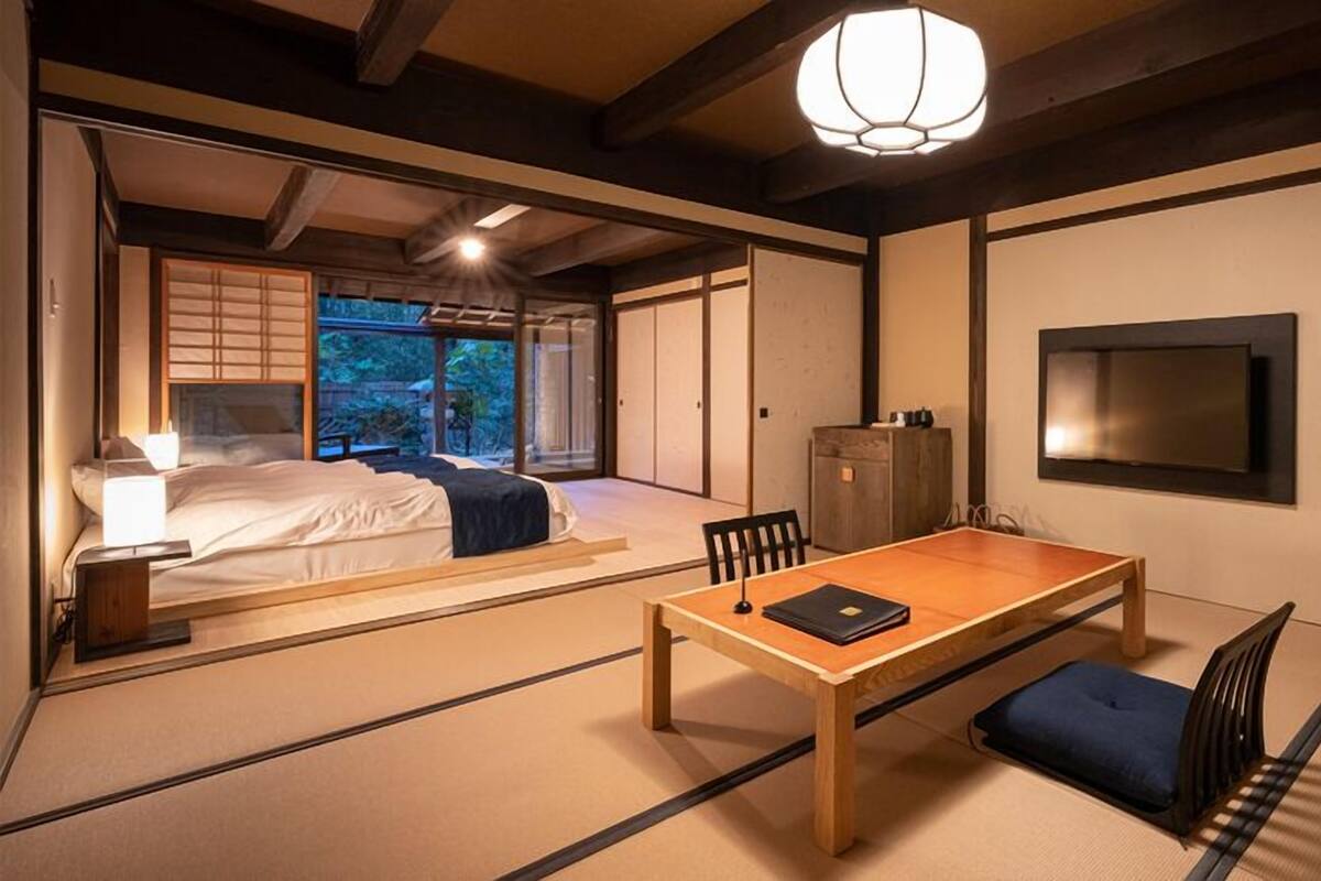A traditional Japanese-style room with tatami flooring, a low table, a bed with a view, and a sliding door leading to a balcony.
