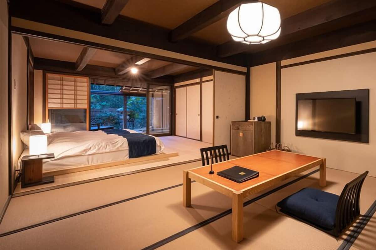 Una habitación tradicional japonesa con suelo de tatami, una mesa baja, una cama con vistas y un fusuma que da a un balcón.