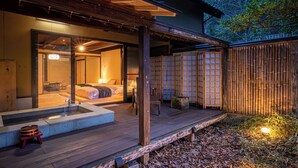 A traditional Japanese-style room with a wooden deck, a hot tub, and a view of the surrounding forest.