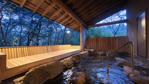A wooden deck with a stone pathway leading to a hot spring area, surrounded by trees.