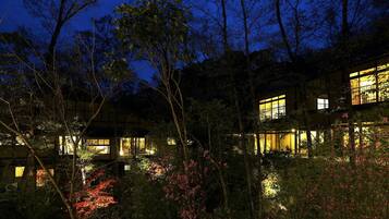 A multi-story building with illuminated windows, surrounded by dense foliage and trees.