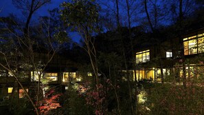 A multi-story building with illuminated windows, surrounded by dense foliage and trees.