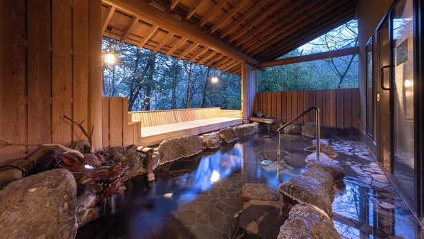 A wooden spa area with a hot spring, wooden benches, and a view of trees.