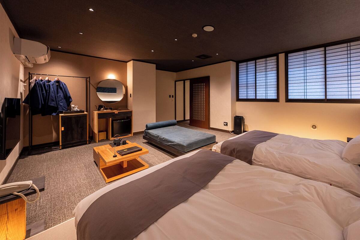 A hotel room with two beds, a desk, a sofa, a wardrobe, and a sliding door.