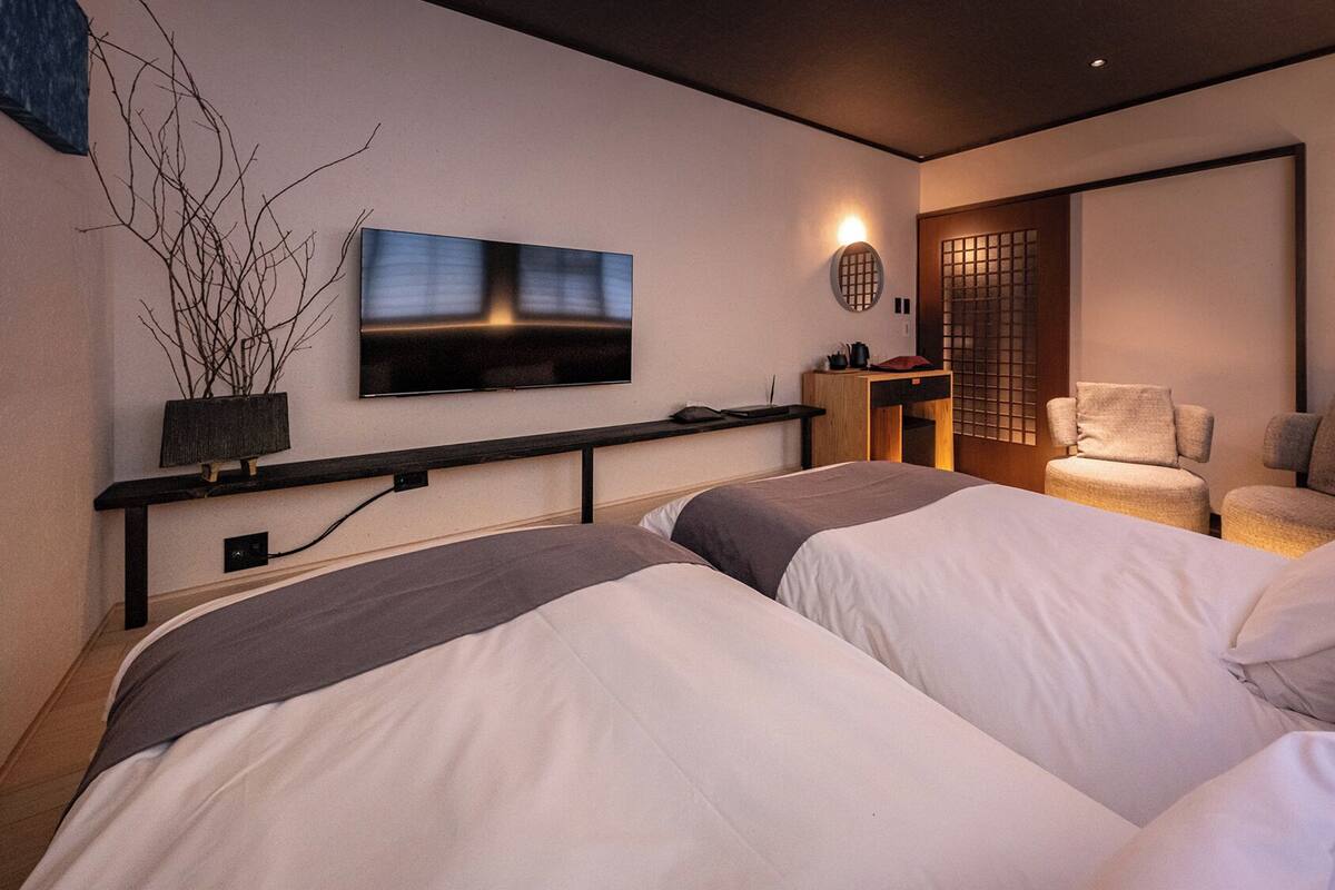 A modern hotel room with two beds, a TV, a desk, and a chair.