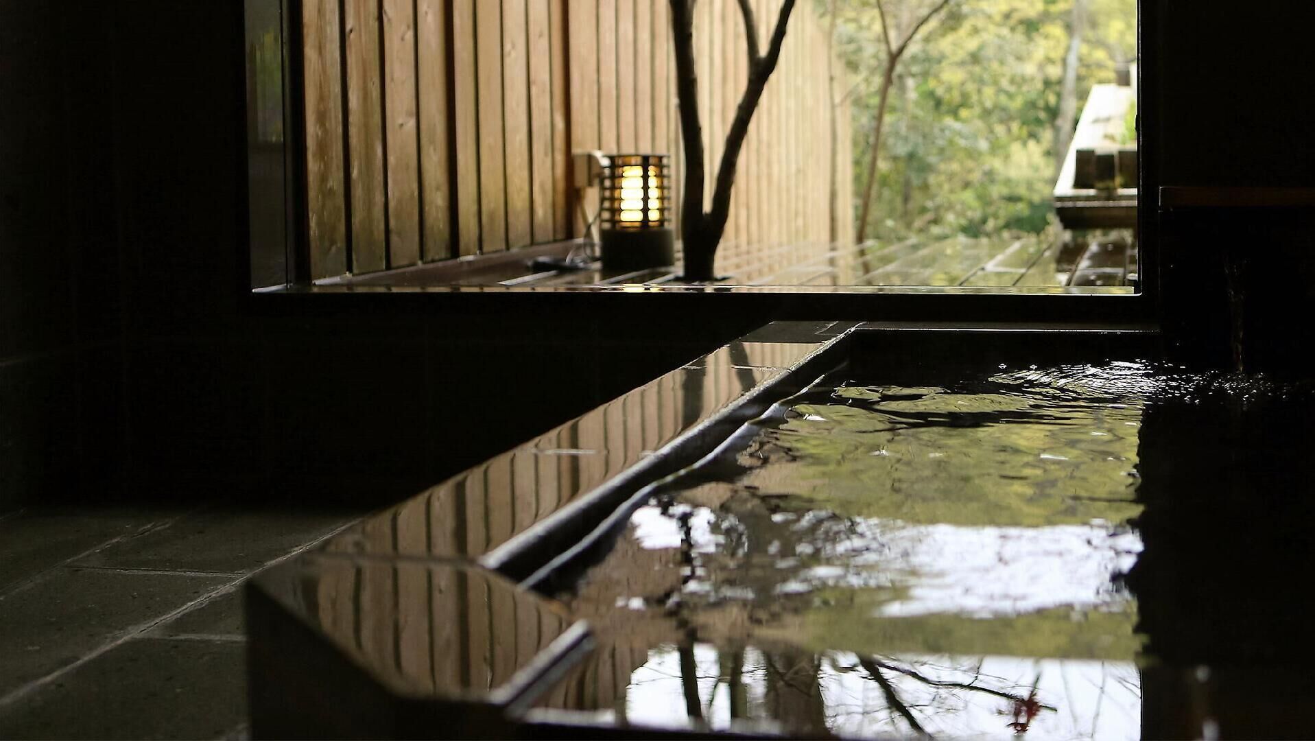 Una tranquila fuente de agua en el interior, con suelo de madera y vistas a árboles a través de una ventana.