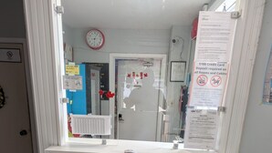A reception area with a white counter, a clock, and a door leading to a room. - Oakwood Motel (Gravenhurst)