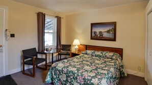 A hotel room with a bed, a desk with a chair, a lamp, and a painting on the wall. - Oakwood Motel (Gravenhurst)