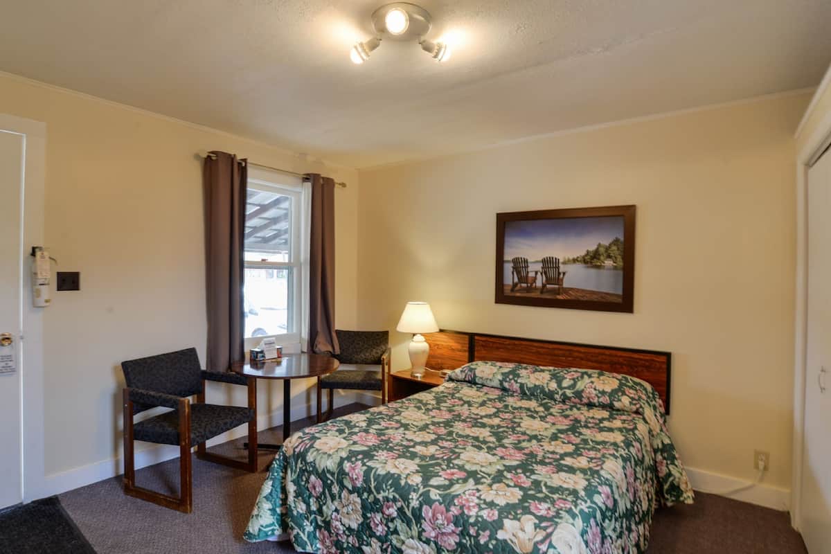 A hotel room with a bed, a desk with a chair, a lamp, and a painting on the wall.