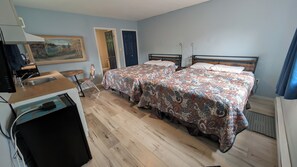 A bedroom with two beds, a wooden desk with a chair, a painting on the wall, and a door leading to another room. - Oakwood Motel (Gravenhurst)