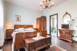 A bedroom with a wooden bed, a nightstand, a dresser, a television, and a chandelier.