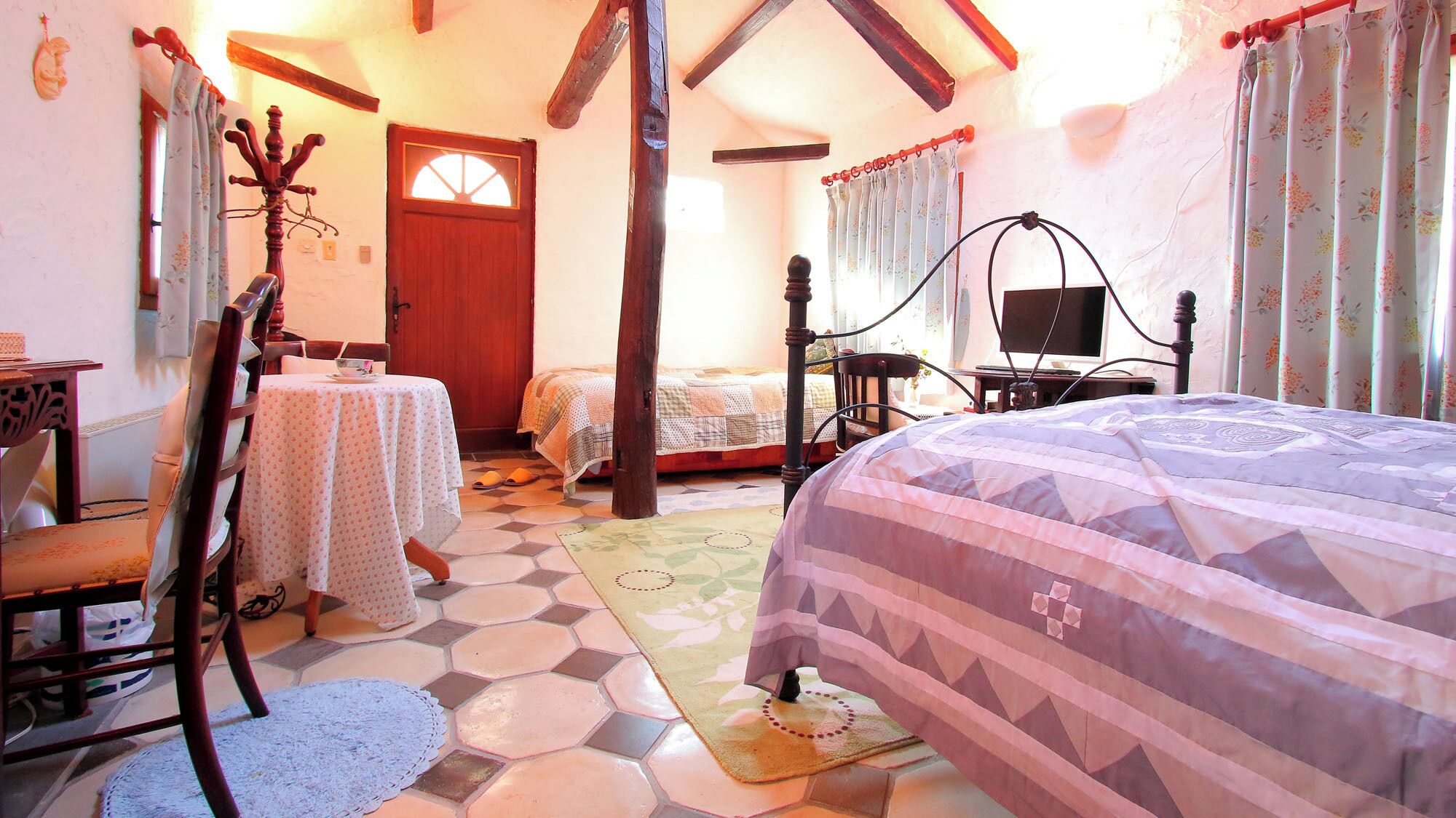 A bedroom with a bed, a chair, a table, a wooden chair, a door, and a window.