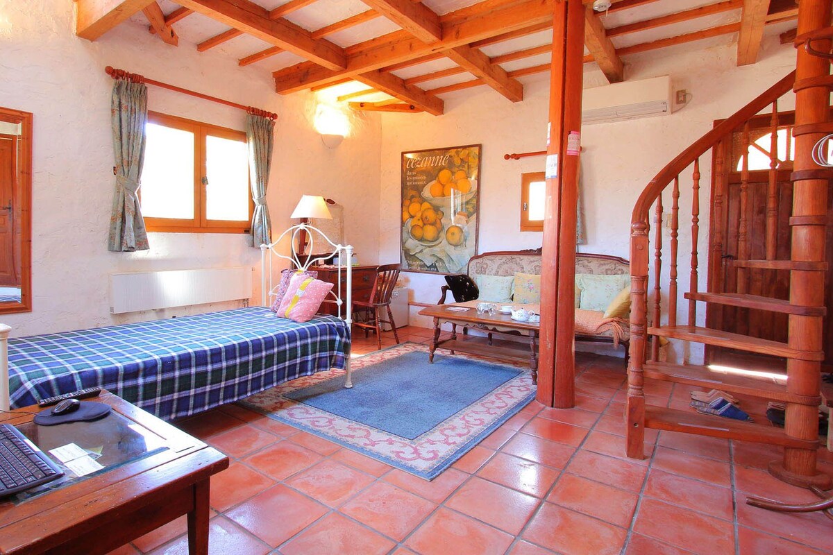 A bedroom with a bed, a desk, a chair, a sofa, a staircase, and a large mirror.